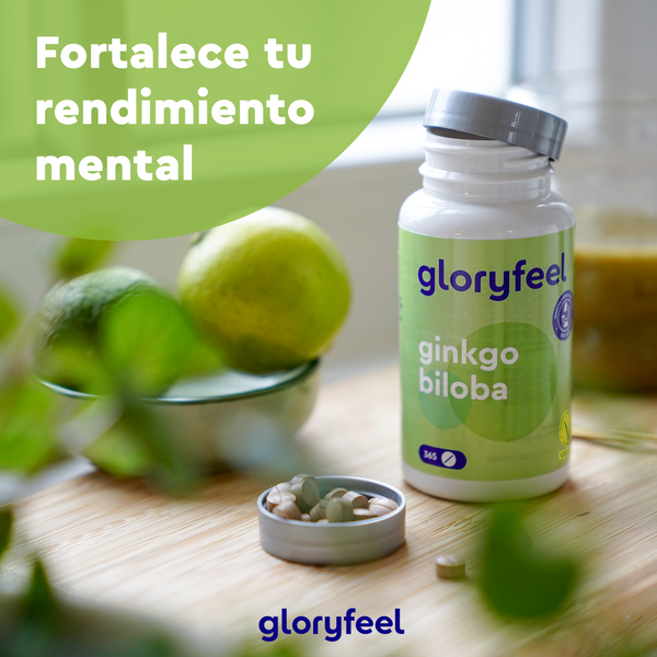 Sobre una mesa hay un frasco de suplemento de Ginkgo Biloba de GloryFeel GmbH España con limas y pastillas en la tapa. El texto en español dice: «Fortalece tu rendimiento mental con el árbol de la vida».