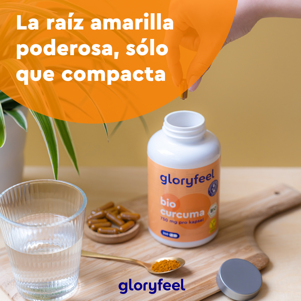 Una mano sostiene una cápsula encima de una botella con la etiqueta &quot;Bio Cúrcuma en cápsulas&quot; de GloryFeel GmbH España, junto a un vaso de agua y más cápsulas. El texto dice &quot;La raíz amarilla poderosa, con curcumina compacta y llena de antioxidantes.