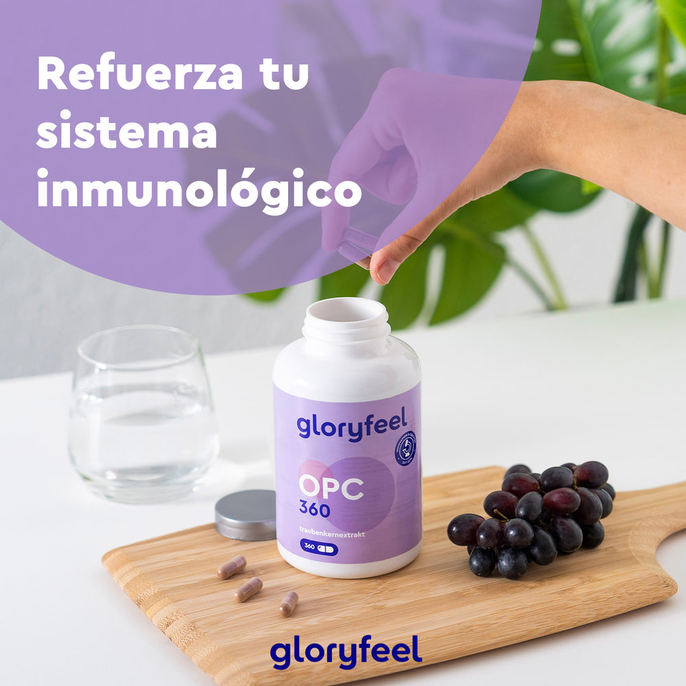 Una persona toma una cápsula de una botella de Gloryfeel GmbH OPC Extracto de semilla de uva 360 cápsulas, rica en antioxidantes, sobre una tabla de madera con uvas y junto a un vaso de agua. El texto en español dice: &quot;Refuerza tu sistema inmunológico con extracto de semilla de uva.