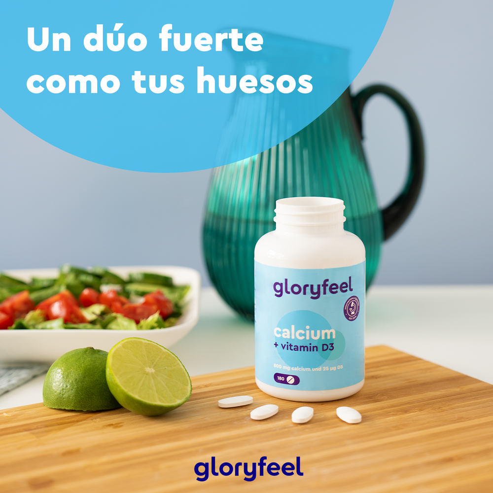 El Calcio + Vitamina D3 de Gloryfeel GmbH descansa en una tabla de madera junto a lima, pastillas, ensalada y una jarra de agua. Texto en español: &quot;Un dúo fuerte como tus huesos.