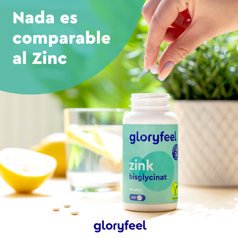 Una mano sostiene una pastilla sobre un frasco con la etiqueta &quot;Bisglicinato de zinc en tabletas&quot; de GloryFeel GmbH, con un vaso de agua y una rodaja de limón al fondo. El texto dice: &quot;Nada es comparable al zinc&quot;, destacando su papel crucial en el metabolismo como suplemento dietético esencial.