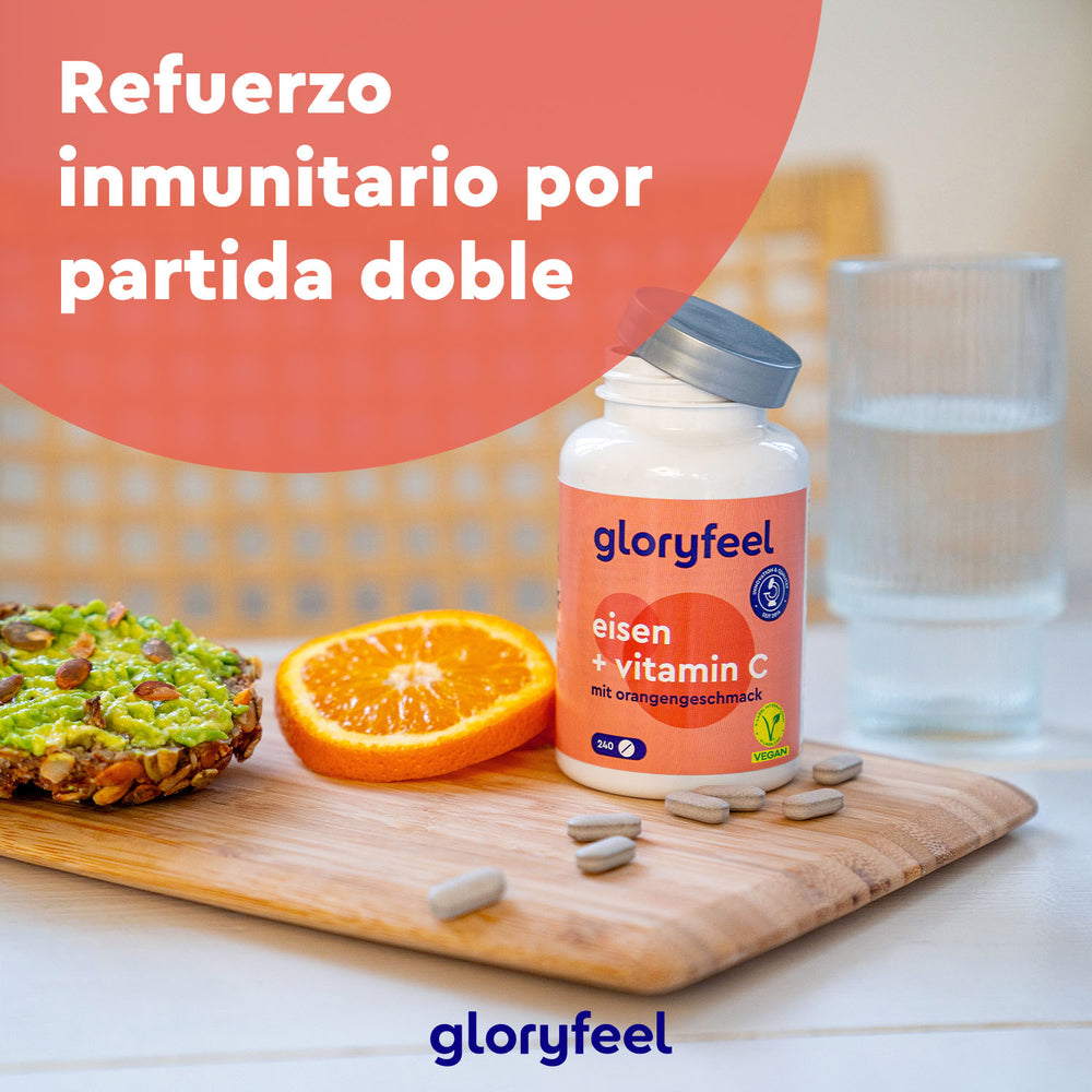 Una botella de GloryFeel GmbH España Hierro + Vitamina C natural se encuentra sobre una mesa con una tostada de aguacate, rodajas de naranja y un vaso de agua. El texto dice: «Refuerzo inmunitario por partida doble».