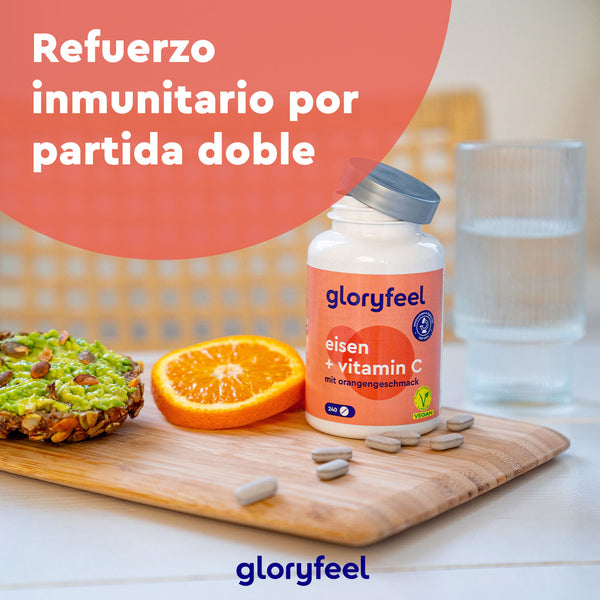 Una botella de GloryFeel GmbH España Hierro + Vitamina C natural se encuentra sobre una mesa con una tostada de aguacate, rodajas de naranja y un vaso de agua. El texto dice: «Refuerzo inmunitario por partida doble».