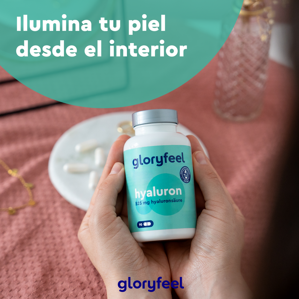Las manos sostienen una botella de Ácido hialurónico Intensivo en cápsulas de GloryFeel GmbH España, con cápsulas y joyas sobre una superficie rosa. Texto arriba: &quot;Ilumina tu piel desde el interior con ácido hialurónico.