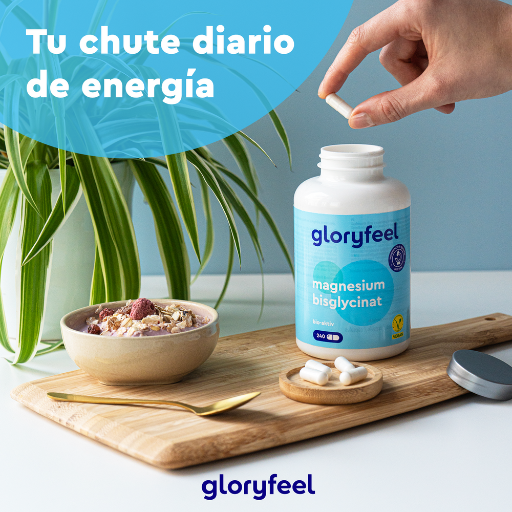 Una mano sostiene una cápsula cerca de una botella de Bisglicinato de magnesio de GloryFeel GmbH España en una bandeja con cereales. El texto dice: &quot;Tu chute diario de energía&quot;.