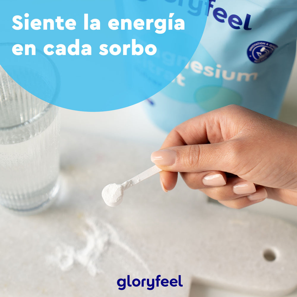 Una mano extrae magnesio en polvo de un pequeño recipiente. Al fondo, un vaso de agua transparente y una bolsa de la marca Gloryfeel GmbH España. El texto en español dice: «Siente la energía en cada sorbo».