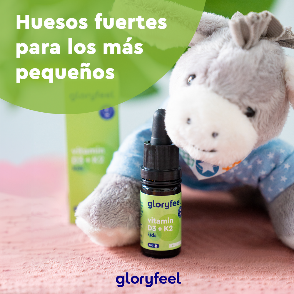 Un burro de juguete junto a una botella de &quot;Vitamina D3 + K2 para Niños en Gotas&quot; de Gloryfeel GmbH, con una caja verde detrás. El texto dice: &quot;Huesos fuertes para los más pequeños.