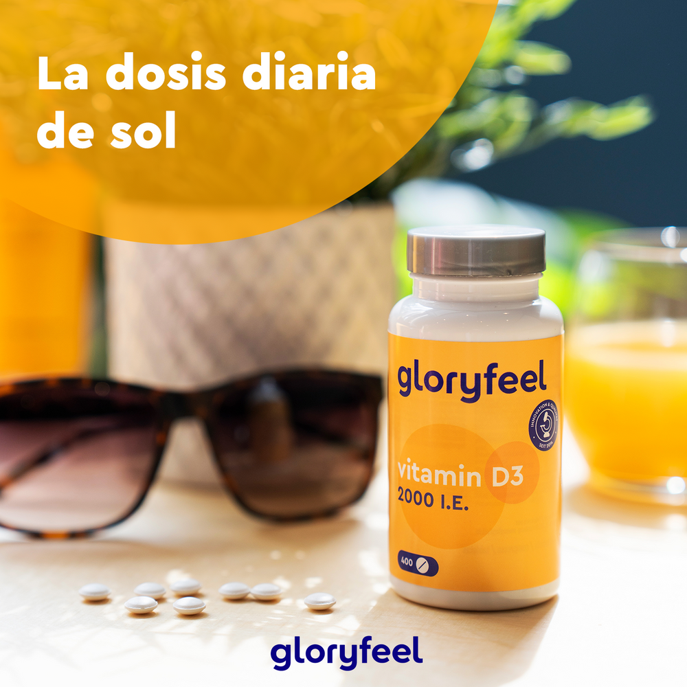 Un frasco de Vitamina D3 2000 UI de GloryFeel GmbH España está sobre una mesa con pastillas esparcidas, gafas de sol, una maceta y zumo de naranja. El texto en español dice: «La dosis diaria de sol», esencial para mantener huesos y dientes sanos.