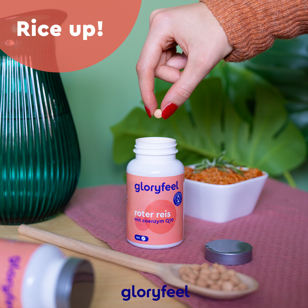 Una mano sostiene una cápsula roja sobre una botella abierta con la etiqueta &quot;Levadura Roja de Arroz con Coenzima Q10&quot; de GloryFeel GmbH España, al lado de un plato de arroz; otra botella yace de lado con el texto &quot;¡Arroz arriba!&quot; en la esquina.