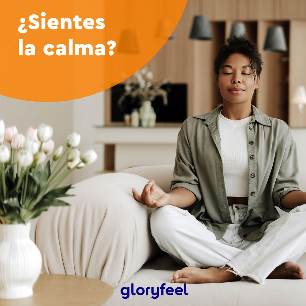 Una mujer medita en un sofá entre exuberantes plantas de interior, irradiando calma. El texto en español, &quot;¿Sientes la calma?&quot;, enfatiza la serenidad que proporcionan la ashwagandha ecológica en cápsulas y el Ayurveda, con el logotipo de GloryFeel debajo.