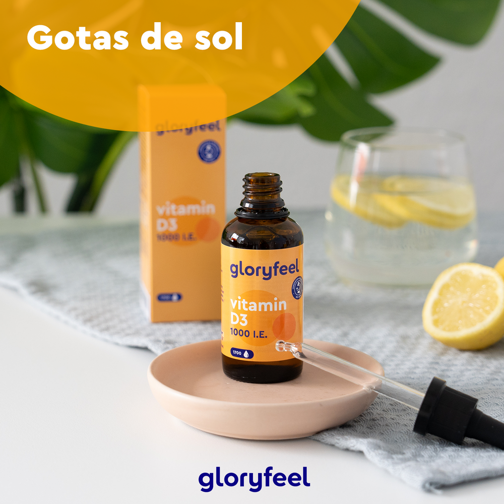 La Vitamina D3 en gotas - 1000 U.I. de Gloryfeel GmbH reposa elegantemente en un plato junto a una refrescante agua de limón y rodajas de limón, resaltando su apoyo al sistema inmunológico, con la botella y la caja realzando la escena sobre una superficie texturizada.