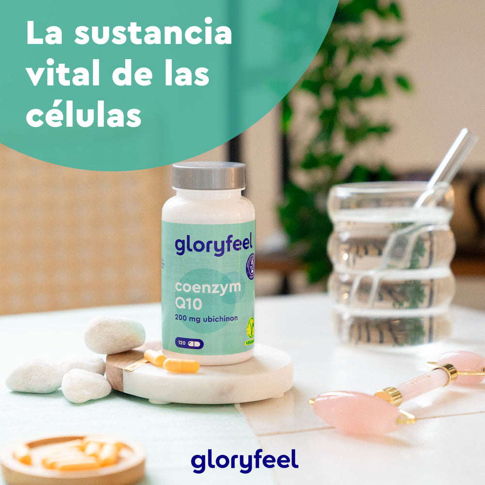 Una botella de GloryFeel Coenzima Q10 descansa sobre una mesa junto a productos para el cuidado de la piel y un vaso de agua, con un texto en español que realza la imagen.