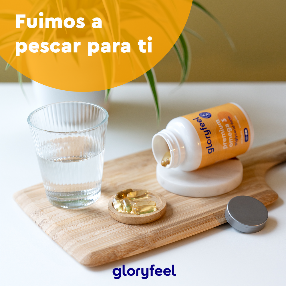 Una botella de Omega 3 en forma de triglicéridos de GloryFeel GmbH España, rico en EPA y DHA, descansa sobre una superficie de madera junto a un vaso de agua y un pequeño plato, con un texto en español que dice: &quot;Fuimos a pescar para ti.