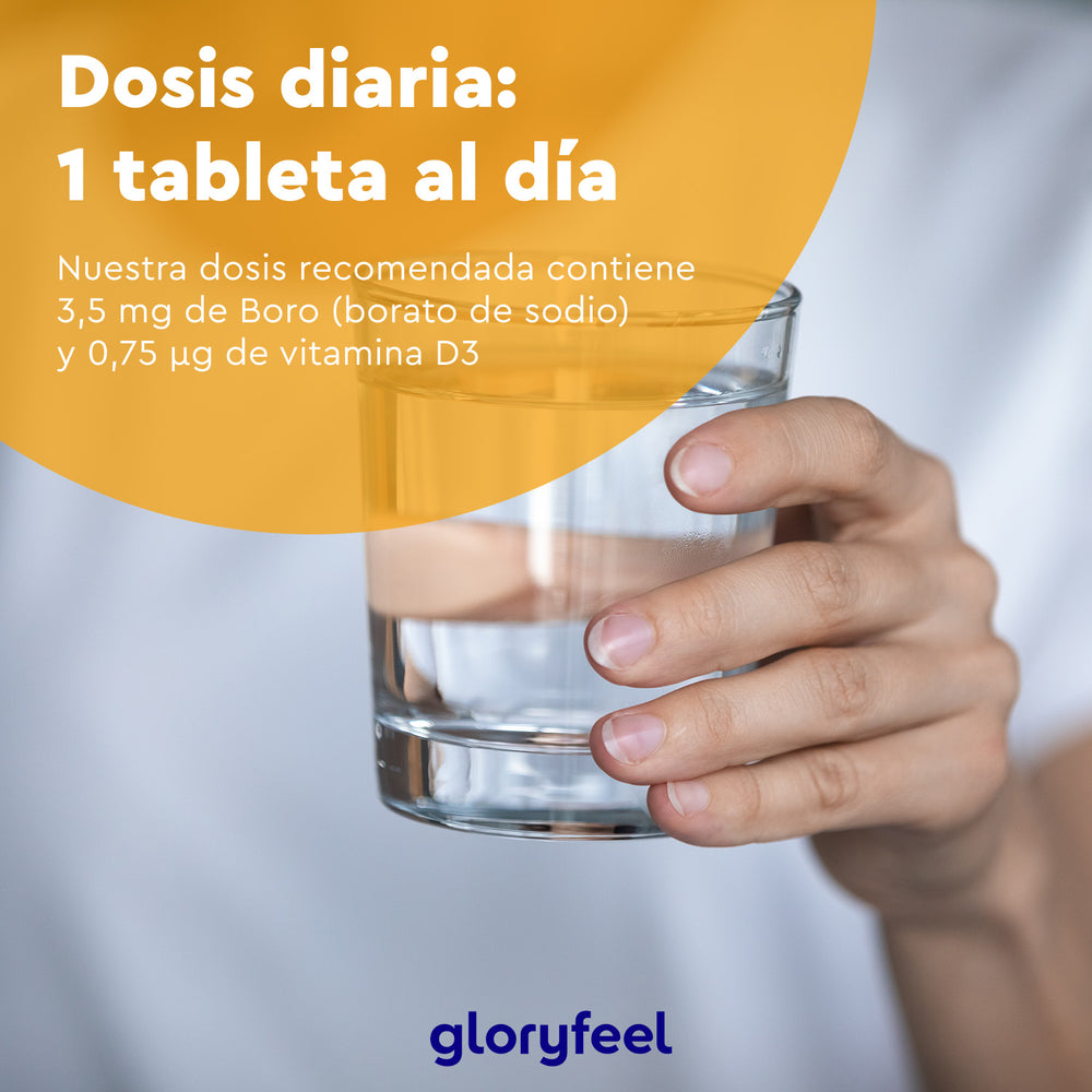 Una mano sostiene un vaso de agua contra un fondo borroso, con un texto en español que muestra la dosis diaria en tabletas de &quot;Boro con Vitamina D3&quot;, resaltando el contenido de boro y vitamina D3 de Gloryfeel GmbH.