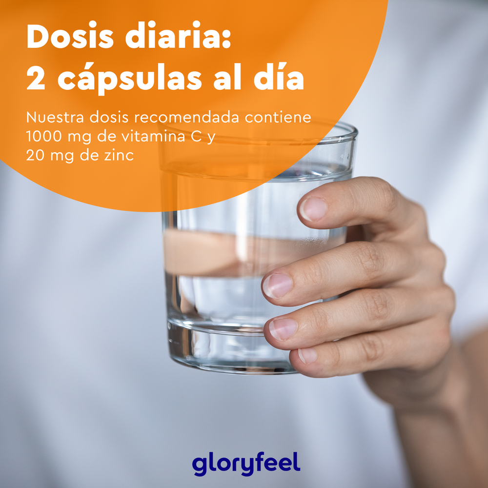 Una persona sostiene un vaso de agua. El texto en español menciona una dosis diaria de 2 cápsulas veganas con 1000 mg de vitamina C tamponada y 20 mg de citrato de zinc. Se muestra la marca &quot;gloryfeel GmbH&quot;.
