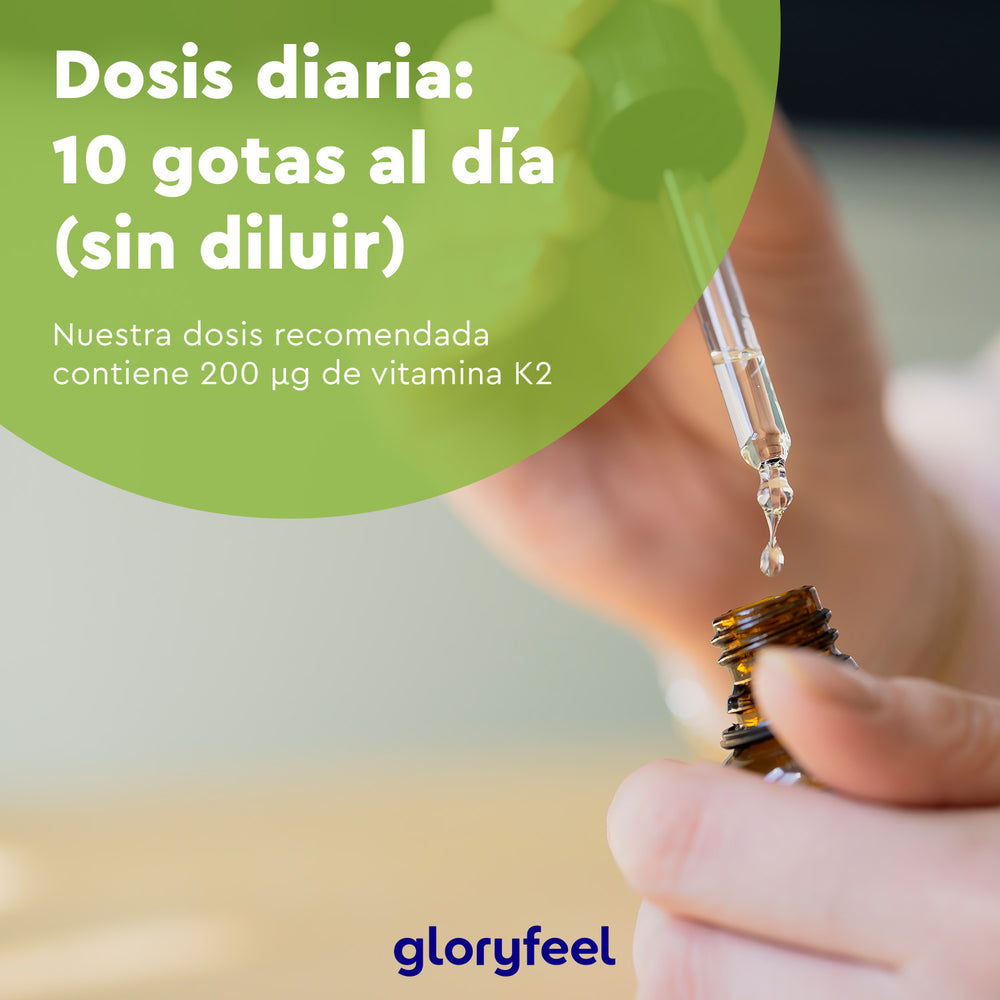 Una mano sostiene un frasco cuentagotas sobre un fondo borroso. Texto: &quot;Dosis diaria: 10 gotas al día (sin diluir). La dosis recomendada de Vitamina K2 Gotas de GloryFeel GmbH Spain contiene 200 µg de vitamina K2, esencial para la formación de huesos saludables.