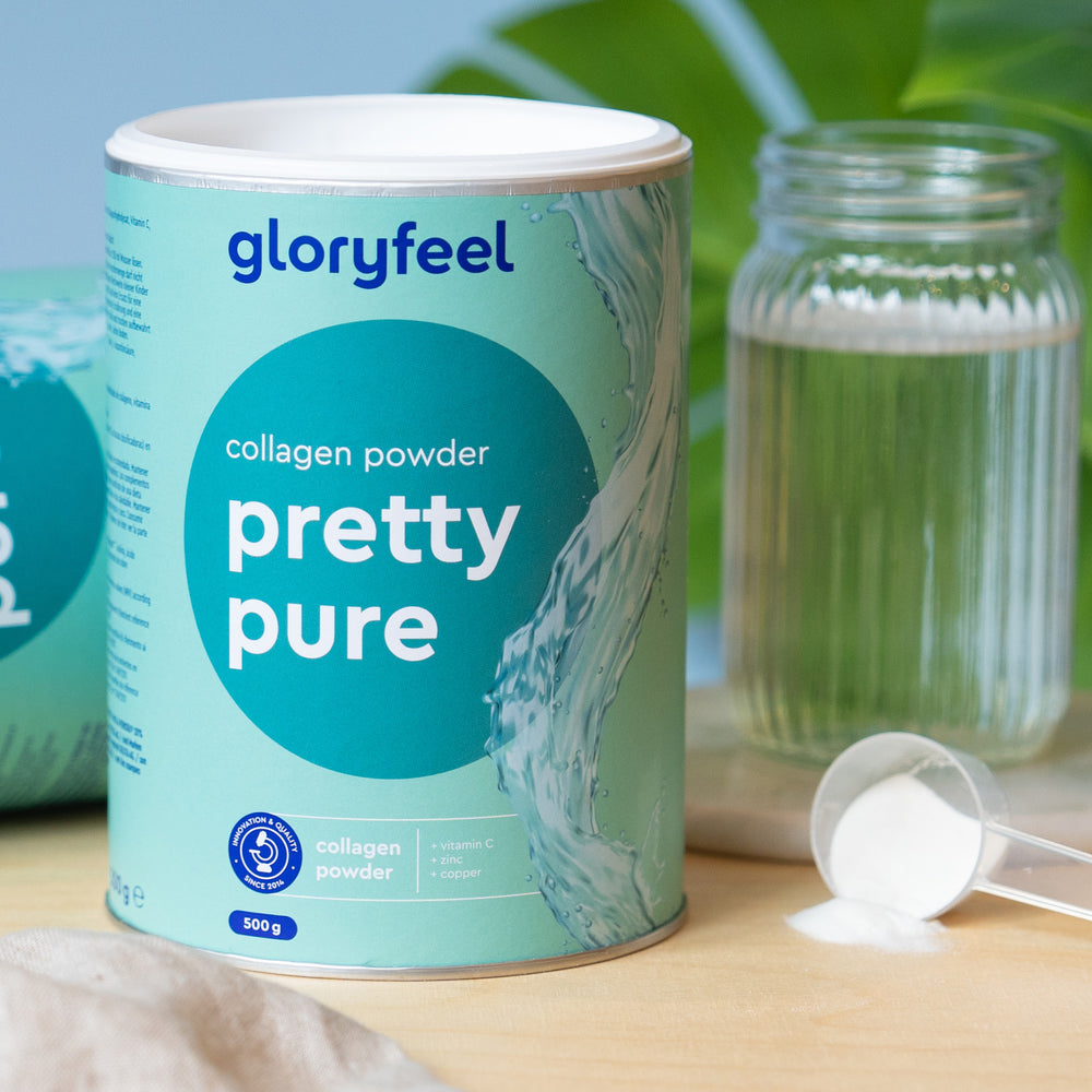 Sobre una mesa hay un bote de Colágeno Marino Hidrolizado en polvo de gloryfeel GmbH España. Junto a él hay un vaso pequeño, una cucharada de polvo y otro bote a un lado.
