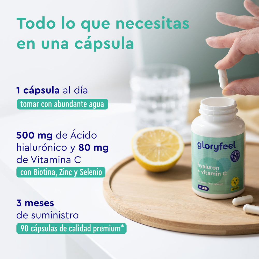 Una mano sostiene un frasco de cápsulas de &quot;Ácido ialurónico con vitamina C&quot; de gloryfeel GmbH España, junto a un vaso de agua y rodajas de limón. El texto destaca la dosis diaria, los ingredientes y el suministro para tres meses.