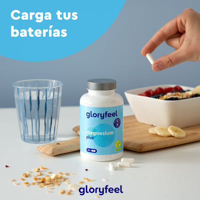Una mano sostiene una cápsula sobre cereales, marcando el comienzo de un día energizante. Sobre la mesa, un frasco de "GloryFeel Magnesio Plus" y cápsulas dispersas resaltan este complemento alimenticio de dicitrato de trimagnesio. El texto dice "Carga tus baterías".