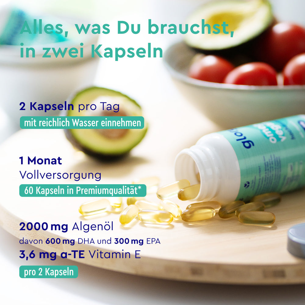 Un envase de cápsulas de Omega 3 + Vitamina E de gloryfeel GmbH España, con información nutricional e instrucciones en alemán, rodeado de aguacates y rodajas de lima sobre una superficie de madera.