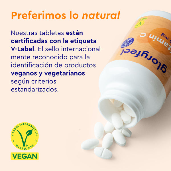 Un frasco de Vitamina C en tabletas de GloryFeel GmbH España, con certificación V-Label para veganos y vegetarianos, refuerza el sistema inmunitario. Hay varias tabletas dispersas cerca.