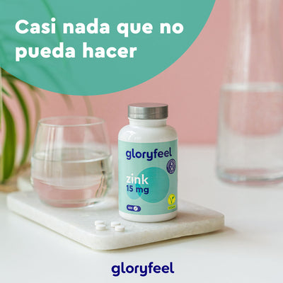 Un frasco de Zinc 15 mg - 400 comprimidos de Gloryfeel GmbH reposa elegantemente sobre una superficie de mármol, junto a tres comprimidos de zinc, un refrescante vaso de agua y una frondosa planta. El texto dice: «Casi nada que no pueda hacer».